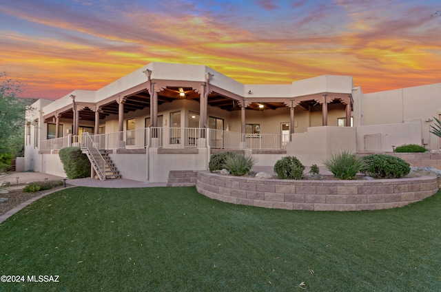 back house at dusk with a lawn and ceiling fan