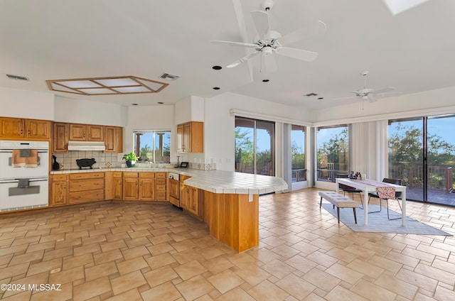 kitchen featuring kitchen peninsula, white double oven, backsplash, and a wealth of natural light