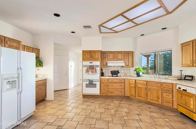 kitchen featuring white appliances, tasteful backsplash, sink, and tile counters