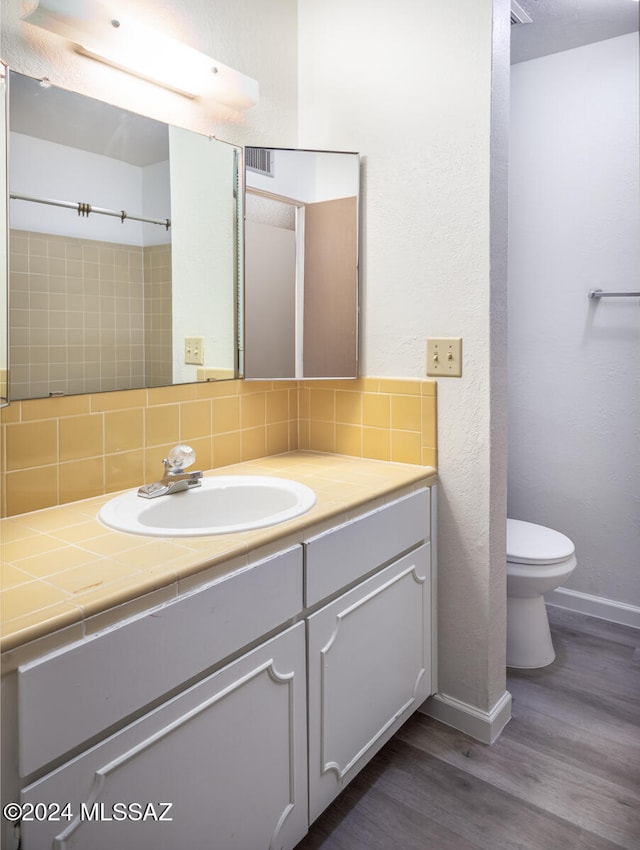 bathroom with vanity, toilet, hardwood / wood-style flooring, and backsplash