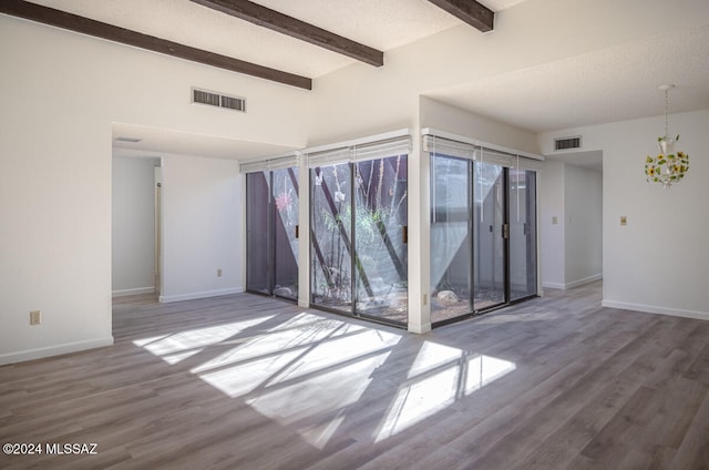 empty room featuring a textured ceiling, beam ceiling, and hardwood / wood-style flooring