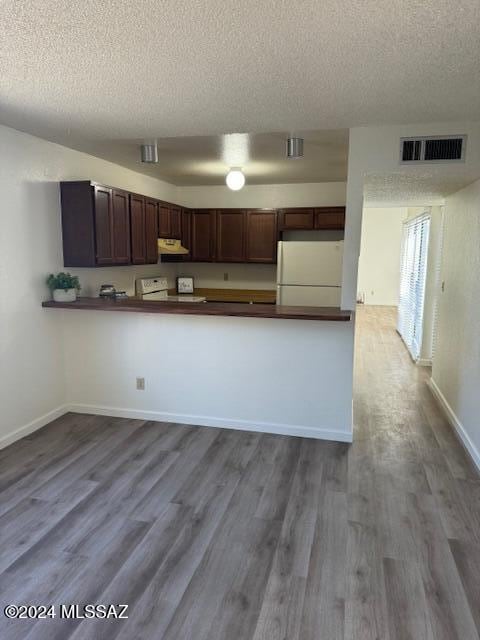 kitchen featuring white appliances, a textured ceiling, kitchen peninsula, and hardwood / wood-style floors