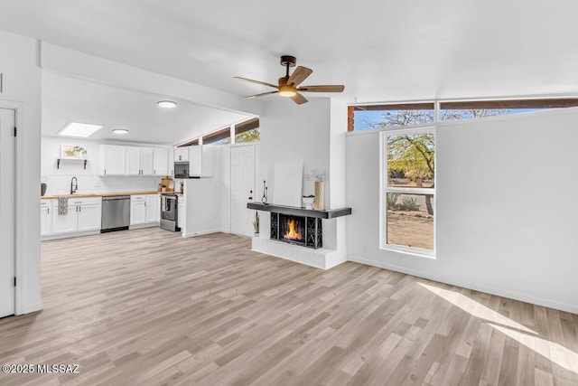 unfurnished living room featuring a ceiling fan, lofted ceiling, a lit fireplace, and light wood finished floors