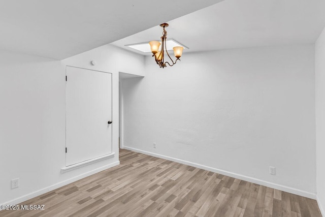 spare room with baseboards, a notable chandelier, and light wood-style floors