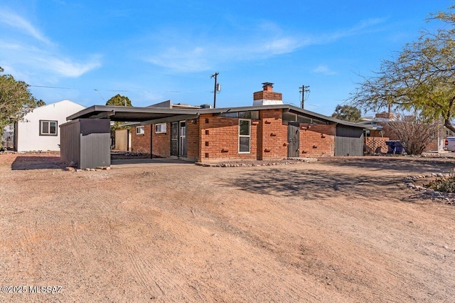 mid-century inspired home with driveway, a chimney, a carport, and brick siding