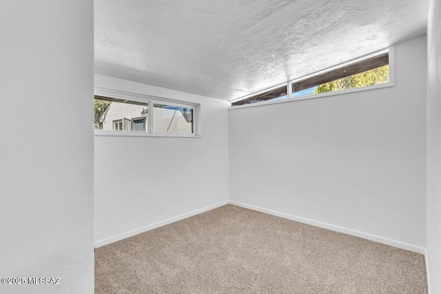 carpeted empty room featuring a wealth of natural light, a textured ceiling, and baseboards