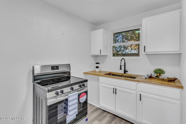 kitchen with butcher block countertops, stainless steel electric range, light wood-style floors, white cabinetry, and a sink