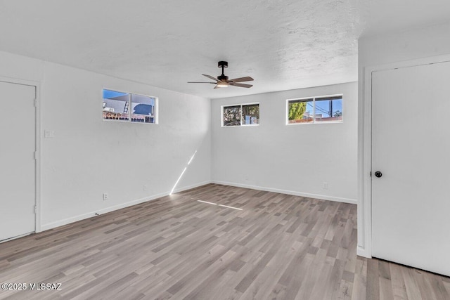 empty room with a textured ceiling, light wood finished floors, a ceiling fan, and baseboards