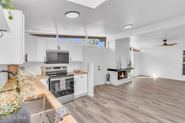 kitchen featuring a warm lit fireplace, stainless steel appliances, butcher block counters, white cabinets, and decorative backsplash