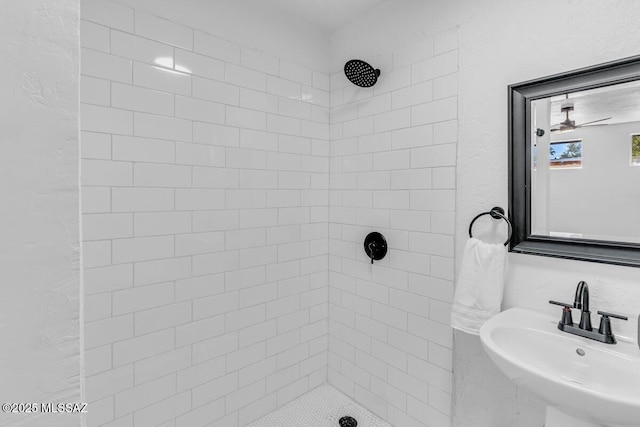 full bath with ceiling fan, a textured wall, tiled shower, and a sink