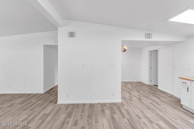 spare room with vaulted ceiling, visible vents, and light wood-style floors