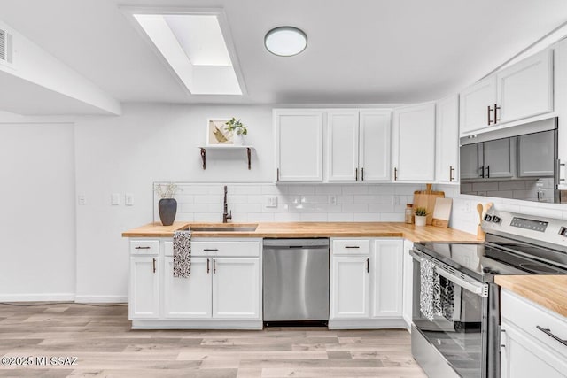 kitchen with butcher block counters, appliances with stainless steel finishes, a sink, open shelves, and backsplash