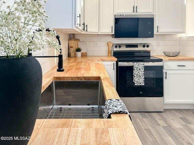 kitchen with decorative backsplash, butcher block counters, wood finished floors, stainless steel range with electric cooktop, and white cabinetry