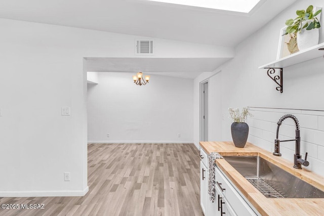 kitchen featuring visible vents, light wood-style flooring, a sink, butcher block countertops, and baseboards