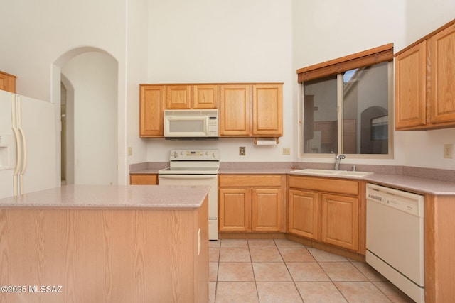 kitchen with sink, a high ceiling, a kitchen island, white appliances, and light tile patterned floors