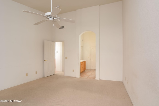 empty room with a high ceiling, light colored carpet, and ceiling fan