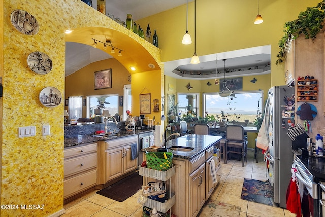 kitchen with dark stone countertops, sink, pendant lighting, light tile patterned floors, and a towering ceiling