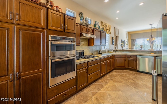 kitchen featuring tasteful backsplash, appliances with stainless steel finishes, hanging light fixtures, light tile patterned floors, and a chandelier