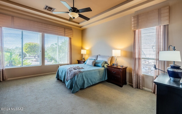 carpeted bedroom with ceiling fan and a tray ceiling