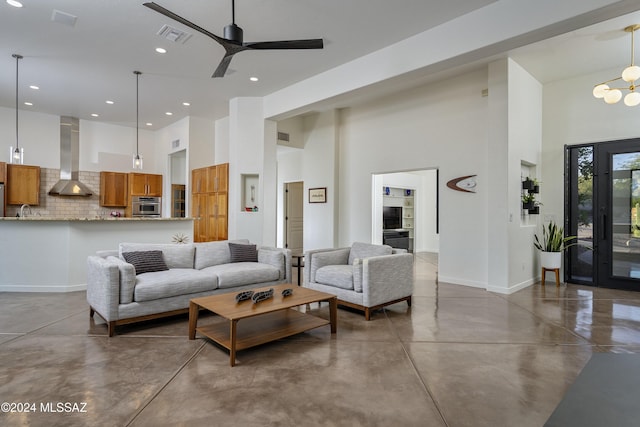 living room featuring concrete flooring, ceiling fan with notable chandelier, a towering ceiling, and sink