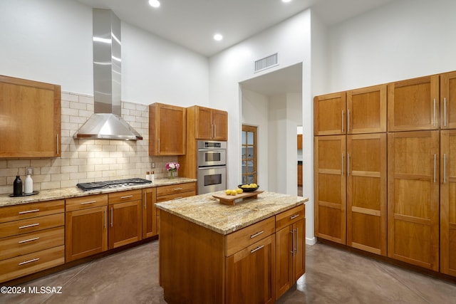 kitchen featuring backsplash, stainless steel appliances, light stone countertops, a kitchen island, and wall chimney exhaust hood