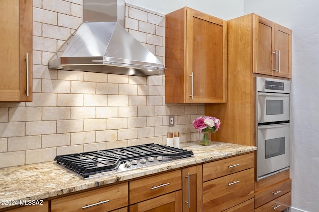 kitchen featuring stainless steel appliances, tasteful backsplash, wall chimney range hood, and light stone counters