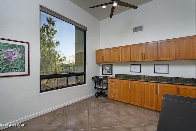 kitchen with dark stone countertops, built in desk, ceiling fan, and a high ceiling