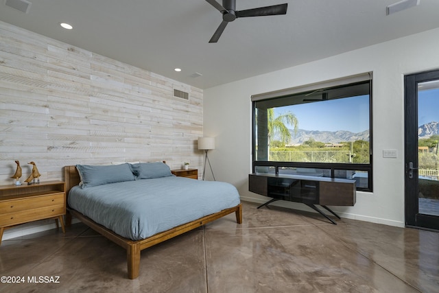 bedroom featuring ceiling fan, access to outside, concrete floors, and wooden walls