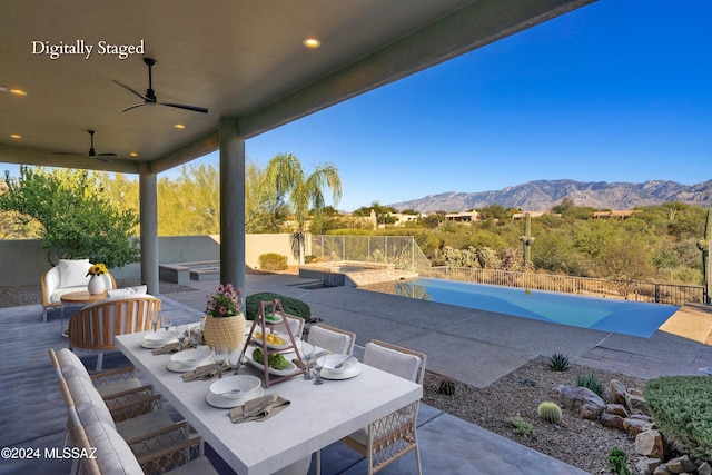 view of patio featuring ceiling fan, a swimming pool with hot tub, and a mountain view