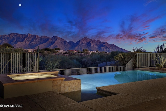 pool at dusk featuring a mountain view and an in ground hot tub