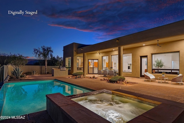 pool at dusk featuring an in ground hot tub, ceiling fan, an outdoor kitchen, and a patio