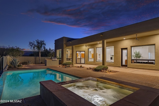 pool at dusk with an in ground hot tub, an outdoor kitchen, ceiling fan, and a patio area