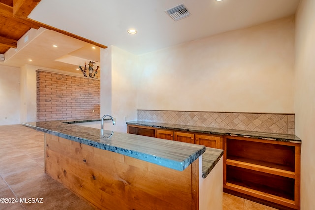 kitchen with decorative backsplash, kitchen peninsula, and light tile patterned floors