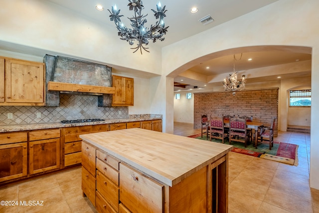 kitchen featuring wooden counters, custom exhaust hood, stainless steel gas cooktop, light tile patterned floors, and a kitchen island