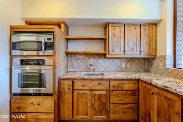 kitchen with light stone countertops, decorative backsplash, sink, and stainless steel appliances