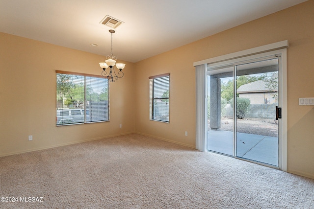 carpeted spare room featuring an inviting chandelier and plenty of natural light