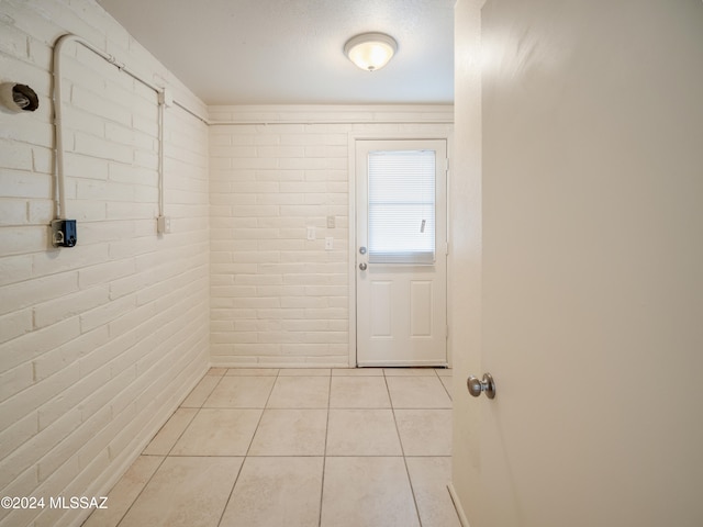 doorway with light tile patterned flooring and brick wall