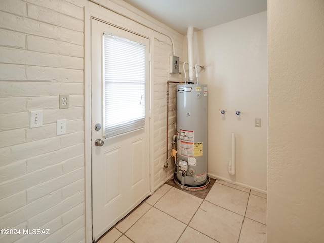 entryway with brick wall, light tile patterned floors, and gas water heater