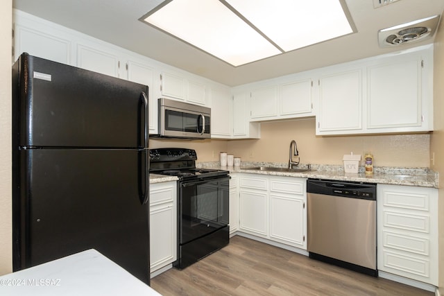 kitchen featuring light stone countertops, a sink, black appliances, white cabinets, and light wood-type flooring