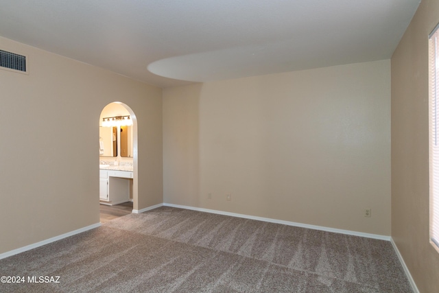 unfurnished bedroom featuring arched walkways, visible vents, carpet floors, and baseboards