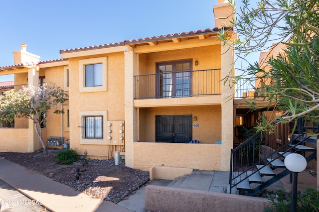 view of front facade with a balcony, fence, a chimney, and stucco siding