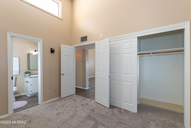 unfurnished bedroom with visible vents, carpet floors, a closet, a towering ceiling, and connected bathroom