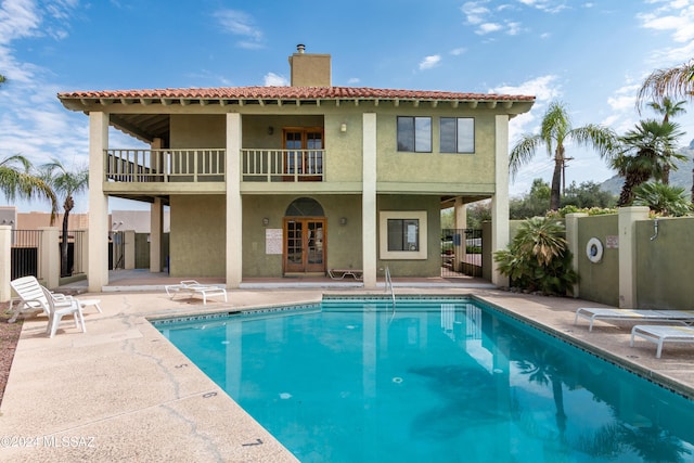 rear view of house with french doors, a patio, a balcony, and a chimney