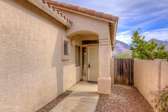 view of exterior entry featuring a tile roof, fence, a mountain view, and stucco siding