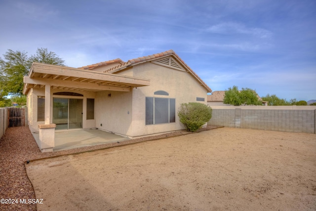 rear view of house with a tile roof, a fenced backyard, a patio, and stucco siding