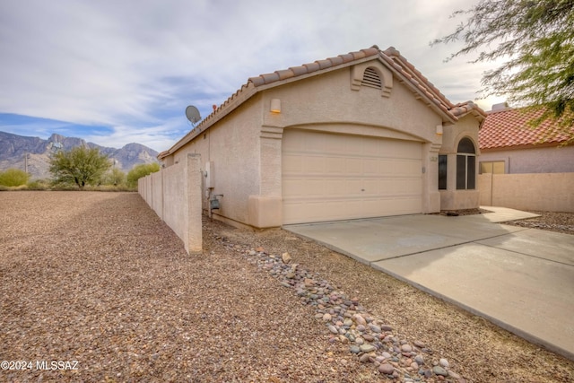 view of side of property with concrete driveway, a tiled roof, an attached garage, a mountain view, and stucco siding