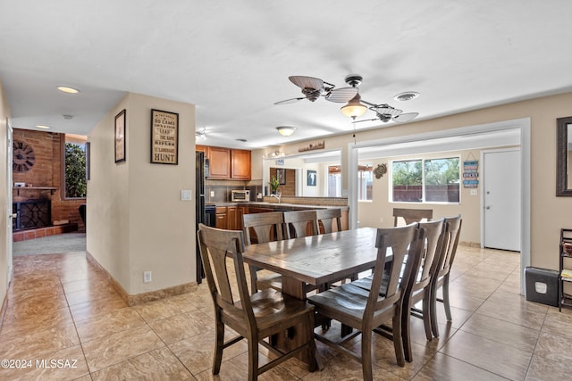 dining space with sink, ceiling fan, light tile patterned flooring, and a fireplace