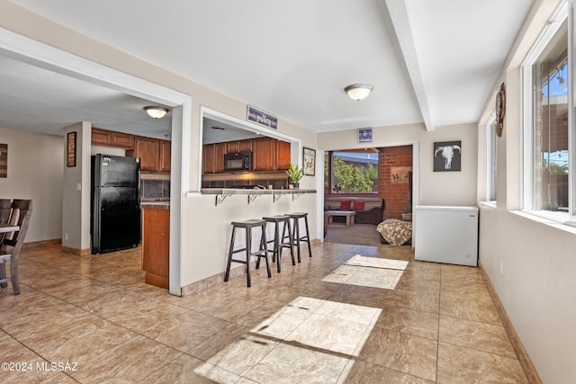 kitchen featuring a breakfast bar area, beamed ceiling, kitchen peninsula, black appliances, and light tile patterned floors