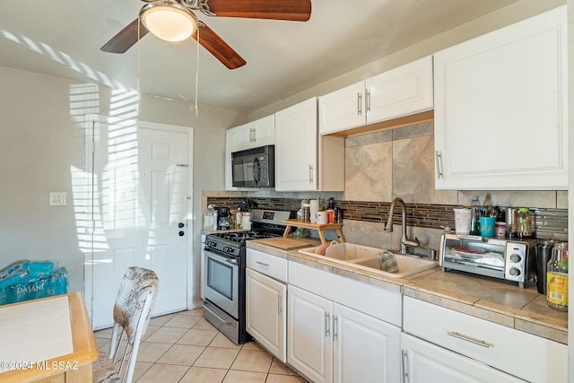 kitchen with gas stove, tasteful backsplash, light tile patterned floors, white cabinetry, and sink