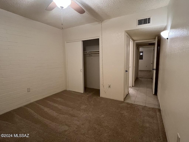 unfurnished bedroom featuring light carpet, a textured ceiling, a closet, ceiling fan, and brick wall